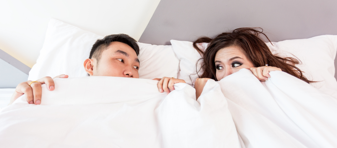 Man en vrouw liggen in bed met de dekens over zich heen getrokken en kijken elkaar vragend aan